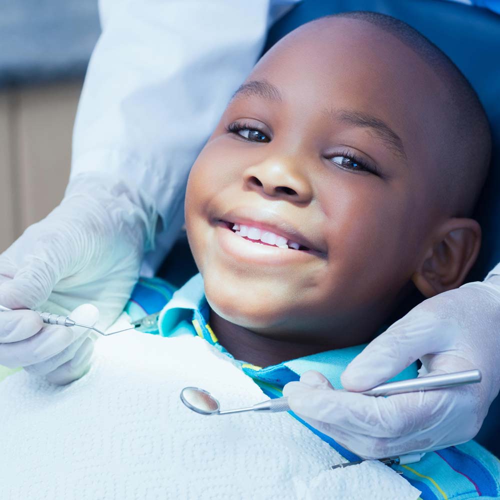 A child smiling while being attended to by a Dentist